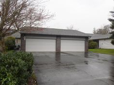 a house with two garages and trees in the front yard on a rainy day