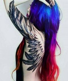 a woman with colorful hair and tattoos on her back is posing in front of a white wall