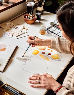 a woman sitting at a table drawing on paper