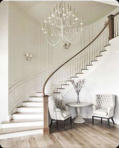 a white staircase with chandelier and two chairs