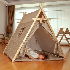 a little boy laying on the floor in front of a teepee tent that is made out of wood