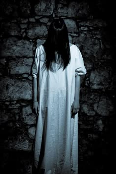 a ghostly woman standing in front of a stone wall with her head down stock photo