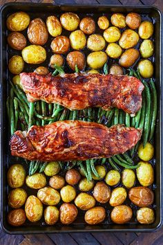 two meats and green beans in a roasting pan with potatoes on the side