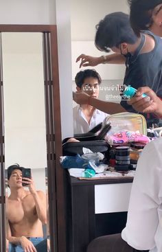 the man is getting his hair done in front of the mirror while another person takes pictures