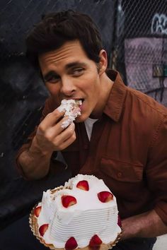 a man eating a large cake with strawberries on the top and white frosting