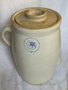 a white ceramic container with a blue seal on the side and a brown lid sitting on a white cloth