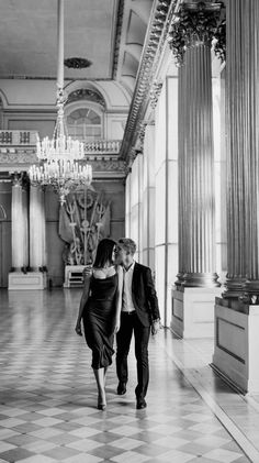 a man and woman walking down a hall holding each other's hands in black and white