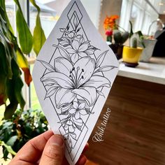 a person holding up a piece of paper with flowers on it in front of some potted plants