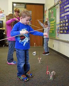 two young boys are playing with string toys in the classroom while another boy looks on