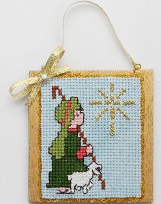 a cross stitch christmas ornament hanging on a wall with a gold ribbon around it