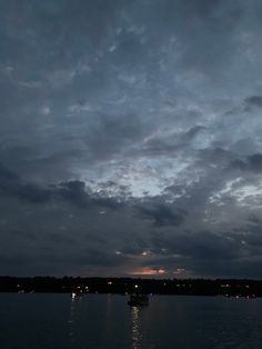 the sky is filled with clouds and boats are out on the water at night time