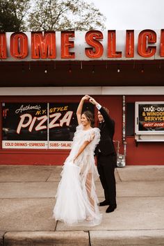 a man and woman are dancing in front of a pizza place with a sign that says home slice