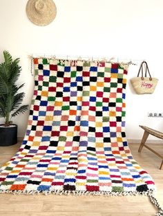 a multicolored blanket sitting on top of a wooden floor next to a potted plant