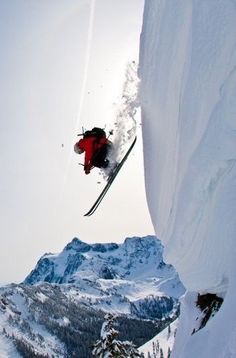 a man flying through the air while riding skis on top of a snow covered mountain