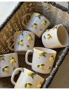 five white mugs with yellow lemons on them sitting in a wicker basket