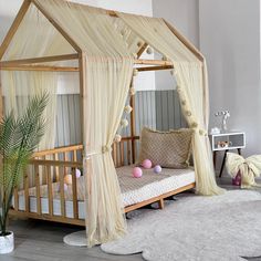 a wooden bed with white drapes and pink balls on the floor next to it