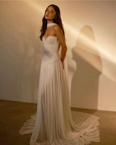 a woman standing in front of a white wall wearing a dress with pleated skirt