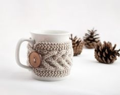 a coffee cup with a button on it next to some pine cones