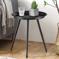 a small black table with two plants on it next to a gray couch and rug