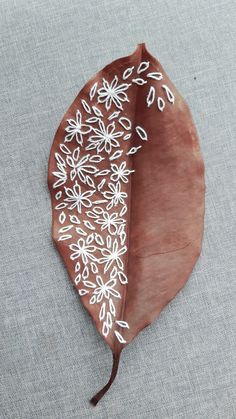 a brown leaf with white flowers on it sitting on a gray tableclothed surface