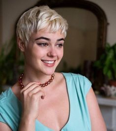 a woman in a blue dress is smiling and holding a beaded necklace on her neck