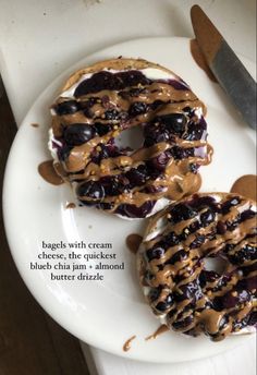 two donuts covered in peanut butter and jelly on a white plate next to a knife