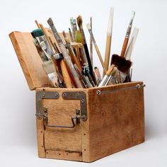 an old wooden box filled with lots of paintbrushes and other art supplies on a white background