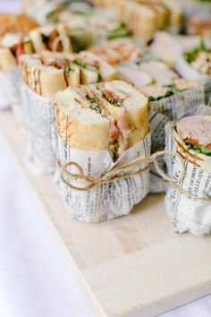 sandwiches wrapped in newspaper sitting on top of a wooden cutting board next to each other