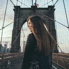 a woman standing in front of the brooklyn bridge with her hair blowing in the wind