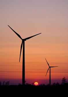 the sun is setting behind three wind turbines