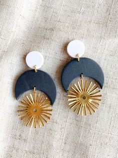 pair of earrings with sun and moon design on them sitting on a linen cloth background