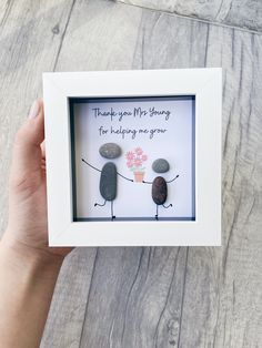 a hand holding a white frame with rocks and flowers in it that says thank you mr stony for helping me grow