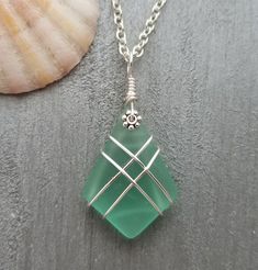 a green glass pendant sitting on top of a silver plate next to a seashell