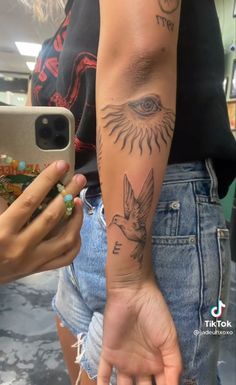 a person with a bird tattoo on their arm holding a cell phone and taking a selfie