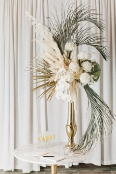 a gold vase filled with white flowers on top of a table next to two champagne glasses