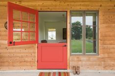 a red door is open in front of a wooden wall and window with an area rug on the floor