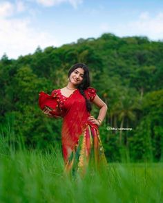 a woman in a red and yellow sari standing in tall grass with her hands on her hips