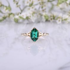 an emerald colored ring with diamond accents on the sides and side stones in the middle