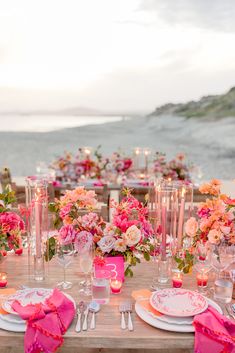 the table is set with pink and white plates, silverware, and flower centerpieces