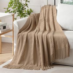 a couch with a blanket on top of it next to a white chair and potted plant