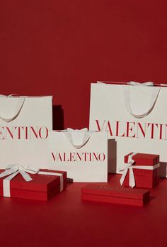 three white shopping bags with red and white ribbon tied around them on a red surface