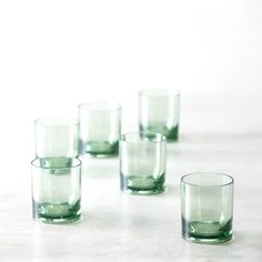 six green glasses lined up on a table with one empty glass next to the other