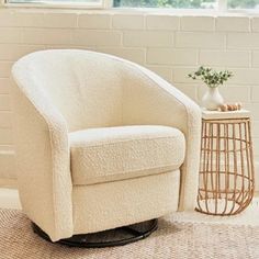 a white chair sitting in front of a window next to a table with a vase on it