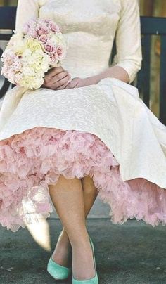 a woman sitting on a bench wearing a dress and holding a bouquet in her hand