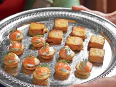 there are many small appetizers on the silver tray in front of someone's hand