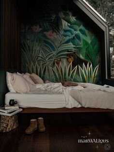 a bed sitting under a window next to a forest mural