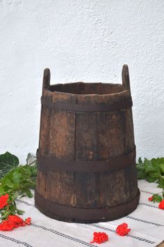 an old wooden bucket sitting on top of a table next to red flowers and greenery