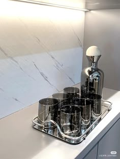 a silver tray with cups on top of it and a bottle in the middle next to it