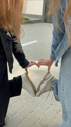 two people holding hands and touching each other's shoes on the sidewalk in front of a building