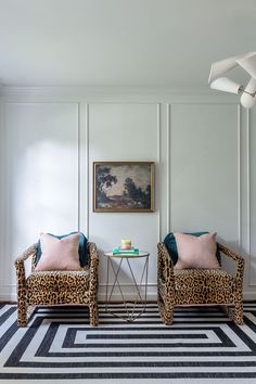 two leopard print chairs sitting next to each other in front of a painting on the wall